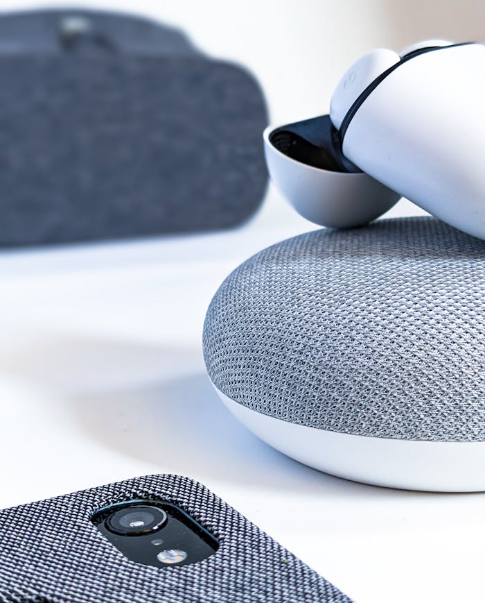 Close-up of wireless earbuds, smartphone, and smart speaker illustrating contemporary tech design.