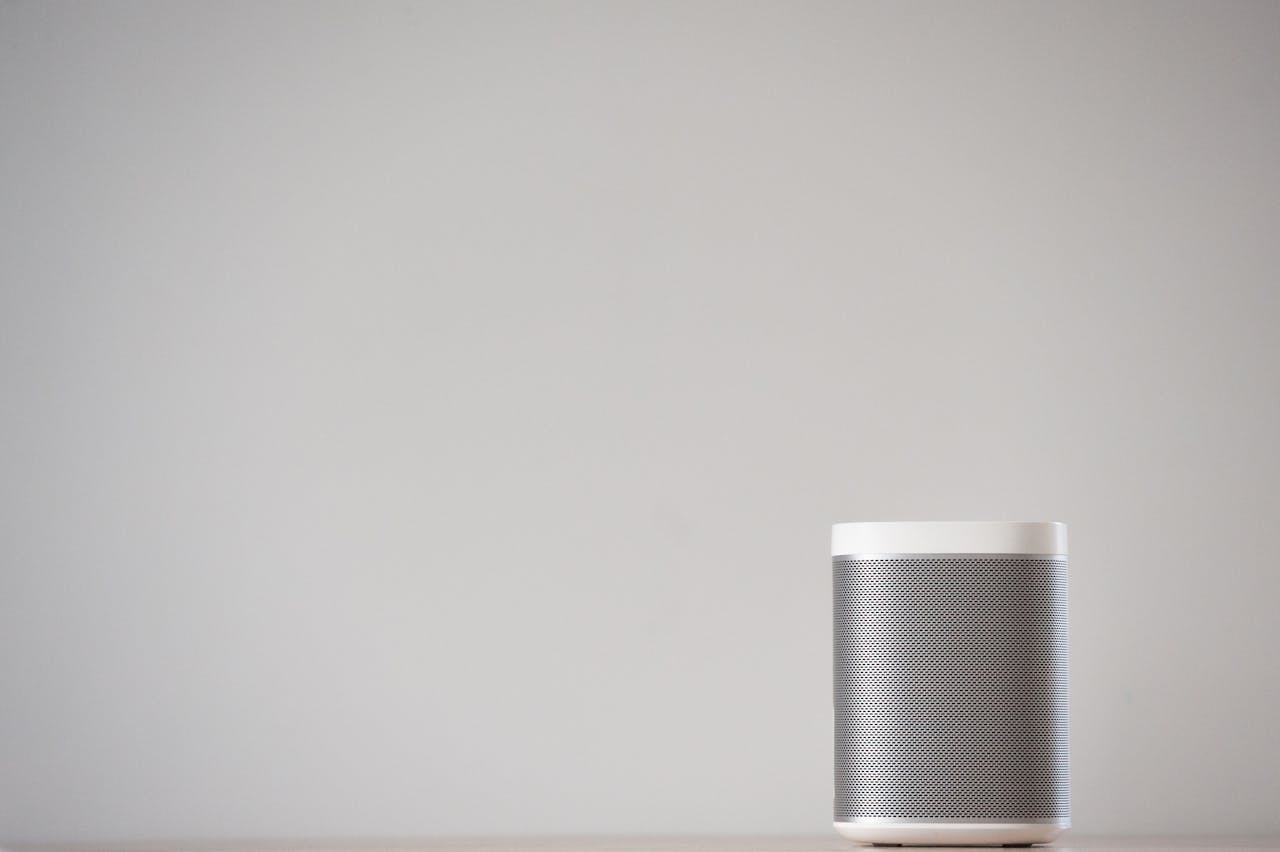 A sleek, wireless smart speaker on a wooden table against a plain wall.